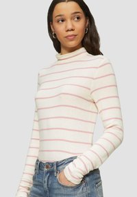 Weißes Langarmoberteil mit rosa horizontalen Streifen, mit einem hohen Kragen und taillierter Passform, kombiniert mit Jeans.