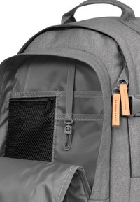 Zaino in tessuto grigio con tasca con zip, compartimento in rete, spallacci regolabili e tirazip in pelle.