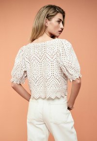 Hvid broderet bluse med pufærmer, dekoreret med udskårne design og bølget kant, båret med højtaljede lyse denimjeans.
