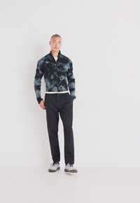 Svart og grå tie-dye jakke med stripete tekstur, med krage og knappelukking. Kombinert med svarte bukser og grå sneakers.