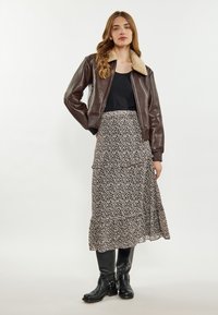 Giacca bomber in pelle marrone con colletto in shearling, abbinata a una canotta nera e a una gonna maxi a balze con motivo floreale. Stivali neri al ginocchio.