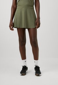Falda de tenis verde en corte A con una textura suave, cintura elástica y un dobladillo acampanado. Combinada con zapatillas deportivas negras y calcetines blancos.
