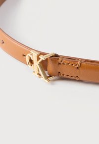 Ζώνη από ταμπά δέρμα με αγκράφα από χρυσό μέταλλο σε σχήμα πλεγμένων γραμμάτων "C" και "K" σε λευκό φόντο.