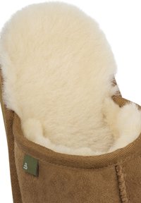 Brown suede slipper with a fluffy cream-colored wool lining. Features a rounded shape and a stitched edge. Small green brand tag visible.