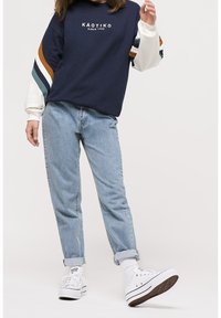 Felpa marina con maniche a strisce multicolori, abbinata a jeans azzurri e sneaker bianche. Look casual, vestibilità rilassata.