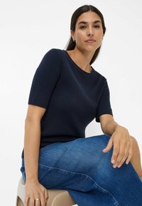Top corto a maniche corte blu navy con scollo rotondo, abbinato a una gonna in denim. Texture liscia, silhouette aderente e design casual.