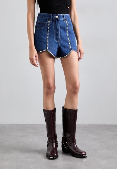 Scurți din denim cu margine cu onduleuri, detalii cu cuie pe părțile laterale, asortați cu cizme burgundii până la genunchi, cu accente de cataramă.