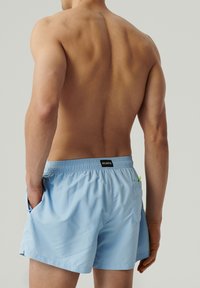 Jasnoniebieskie szorty kąpielowe z elastycznym paskiem w talii, bocznymi kieszeniami oraz detalem kieszeni z tyłu. Wykonane z gładkiego, lekkiego materiału.