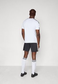Herresportdrakt med hvit kortermet skjorte, svarte shorts med striper, hvite knelang sokker og svarte sko.