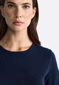 Un pull bleu marine avec un col rond, une texture côtelée et un tissu doux, présenté sur un fond clair.