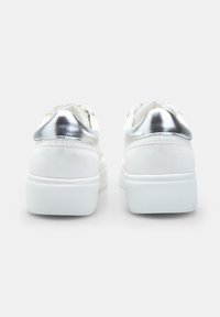 Baskets blanches avec une tige en cuir lisse et des accents argentés au niveau du talon. Semelle en caoutchouc blanc épais avec un motif de grip texturé.