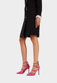 Sandali con tacco alto in pelle sintetica rosa, con più cinturini alla caviglia, design open-toe e punta quadrata. Texture liscia, finitura elegante.