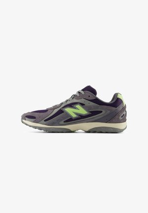 Chaussure de sport grise et violette avec un logo "N" vert sur le côté, dessus en mesh et en daim, et semelle en caoutchouc grise.