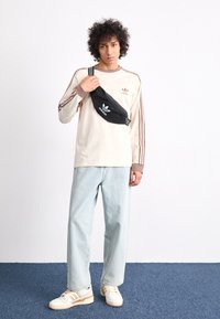 Ανοιχτό μπεζ πουκάμισο με μακριά μανίκια και καφέ ρίγες, σε συνδυασμό με ανοιχτό μπλε τζιν και κρεμ αθλητικά παπούτσια με κρεμ και χρυσές λεπτομέρειες. Μαύρη τσάντα χιαστί.