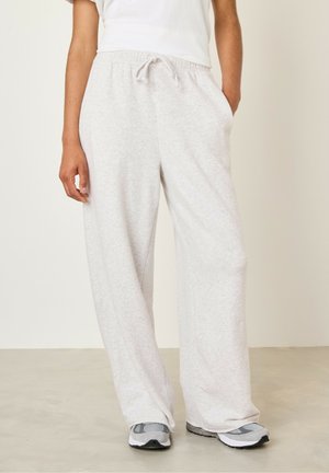 Pantalon de survêtement doux, gris clair, avec une coupe décontractée, une taille avec cordon de serrage et des poches latérales. Porté avec des chaussures de sport grises.