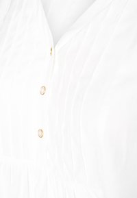 Abito bianco con pieghe verticali, bottoni rotondi dorati e una parte inferiore arricciata. Tessuto morbido con una texture liscia.