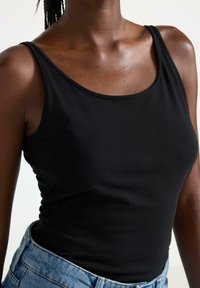 Sort ærmeløs tanktop lavet af glat, strækbart stof med rund hals, parret med højtaljede lys blå denimbukser.