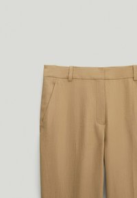 Pantaloni color sabbia con una finitura liscia e testurizzata, due tasche laterali e un design a gamba dritta con vita piatta.