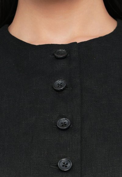 Black linen garment with a round neckline, featuring five black buttons down the front, displaying a textured fabric and simple design.