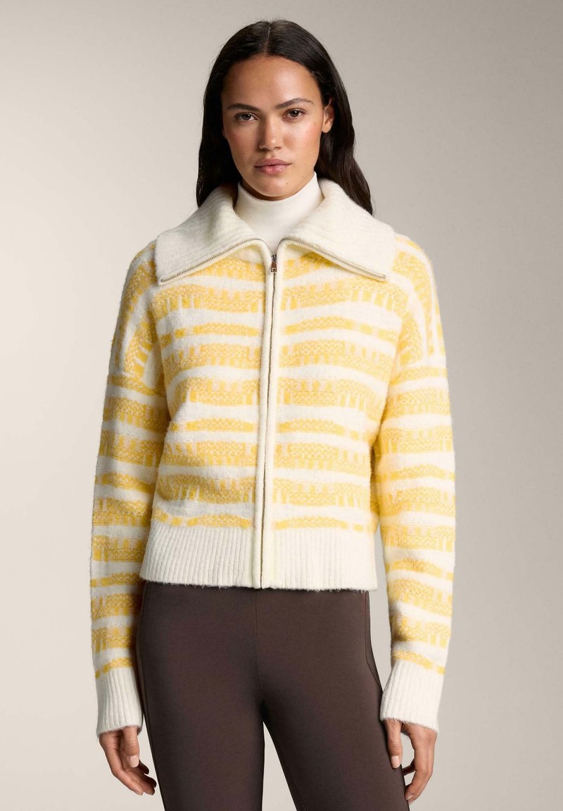 Cardigan en maille crochet avec un motif à rayures jaunes et blanches, doté d'un large col et d'un ourlet côtelé. Le matériau semble doux et texturé.