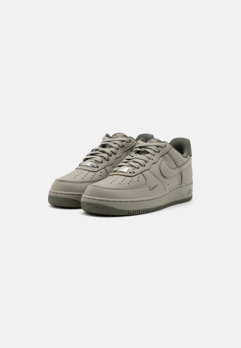 Zapatillas de cuero gris con puntera perforada, textura suave, cordones redondos y suela de goma con un patrón texturizado. Logotipo de Nike presente.