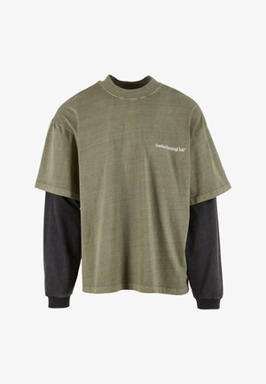 T-shirt verde oliva a maniche corte sovrapposto a una maglietta nera lunga. Presenta un collo rotondo e il testo bianco "Sunday Running Club" sul petto.