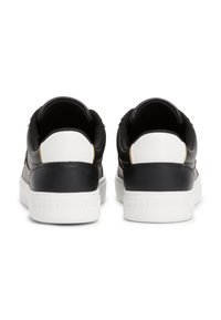 Sneaker in pelle bianca e nera con un design testurizzato, dotati di una suola bianca uniforme, dettagli a contrasto sul tallone e marchio in rilievo sul retro.