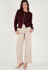 Cardigan bordeaux à boutons en tricot doux, pantalon large crème mi-long, et mules beiges à talons avec un accent décoratif.