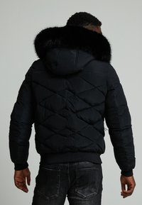 Giubbotto puffer nero con cappuccio bordato in pelliccia nera e design a rombi, dotato di polsini a coste e vita sagomata.