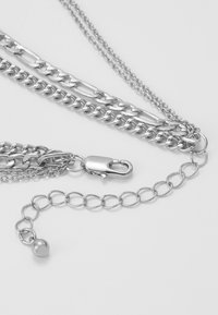 Collier en chaîne argent comprenant plusieurs styles de maillons, un fermoir à homard et un petit détail en perle ronde.