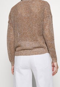 Pull en tricot avec un motif marron et crème, doté d'une coupe décontractée, de poignets côtelés et d'un ourlet uni, associé à un pantalon large blanc.