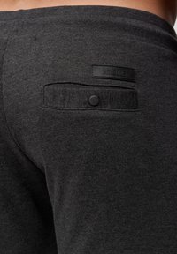 Sorte bomulds joggers med en baglomme med knaplukning og et mærket patch-label. Blød tekstur med en glat overflade.