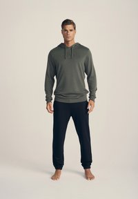 Completo maschile composto da una felpa a maniche lunghe verde oliva con tasca frontale e coulisse regolabili, abbinata a pantaloni neri.