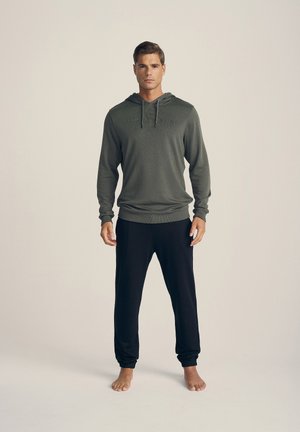 Herenoutfit met een olijfgroen hoodie met lange mouwen, een voorzak en verstelbare trekkingkoordjes, in combinatie met zwarte broek.