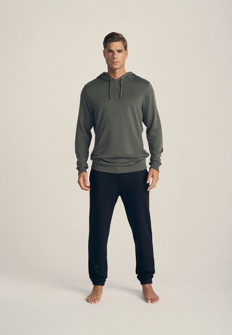 Completo maschile composto da una felpa a maniche lunghe verde oliva con tasca frontale e coulisse regolabili, abbinata a pantaloni neri.