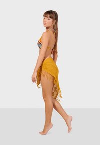 Pestrý bikini top s vzorom a žltou sukňou so strapcami. Sukňa má textúrovaný dizajn a je previazaná v páse.
