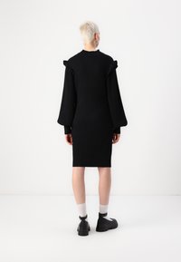 Black ribbed knit dress with puffed sleeves, fitted silhouette, and a crew neckline. Model is wearing black shoes and white socks.
