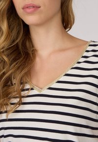 T-shirt à col V rayé présentant des rayures horizontales bleues marines et blanches, avec une bordure métallique dorée le long de l'encolure et en tissu en coton doux.