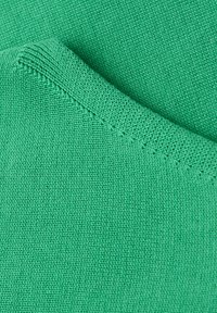 Gros plan sur un tissu tricoté vert montrant une texture détaillée et une couture pliée.