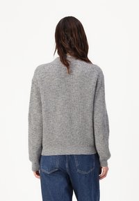 Maglione grigio a coste con collo alto, caratterizzato da maniche lunghe e orlo aderente, abbinato a jeans in denim blu. Dettaglio di lavorazione a maglia testurizzata.