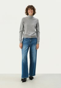 Lys grå turtleneck sweater, løstsiddende blå jeans og sorte hæle med sløjfe detaljer. Glat tekstur; afslappet, casual stil.
