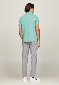 Camisa de polo turquesa con cuello, combinada con pantalones gris claro. Zapatillas blancas con acentos en rojo y azul marino. Vista desde la parte posterior.