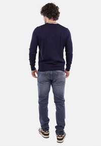 Maglione blu navy con polsini e orlo a coste, abbinato a jeans azzurri e sneakers marroni. Vista posteriore che mostra la vestibilità e la texture del capo.
