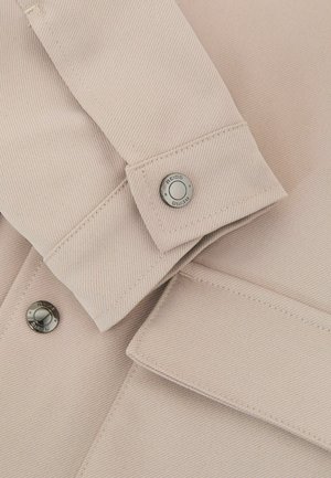 Beige bomuldsjakke med mønster af nålestriber, der har en knap med "REISS"-mærke på et ærme og rene syningsdetaljer.
