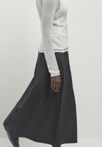 Gonna nera dal design fluido, realizzata in un tessuto leggero. Abbinata a una maglia bianca a maniche lunghe aderente e lavorata a trama.