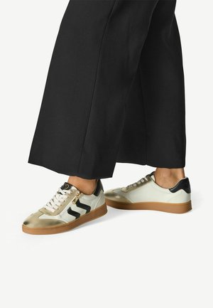 Baskets arborant un design noir et or métallique, avec des lacets blancs et des semelles en caoutchouc beige ; matériaux en cuir et synthétiques utilisés.