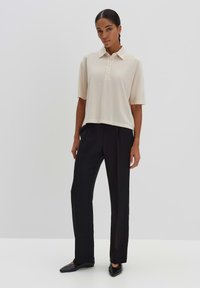 Polo en crème avec un col et une patte de boutonnage, associé à un pantalon noir ajusté et des ballerines noires. Tissu lisse avec une coupe décontractée.