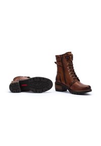 Des bottines en cuir marron présentent un laçage à l'avant, une fermeture éclair sur le côté, un talon empilé et une semelle en caoutchouc texturée avec un motif en étoile.