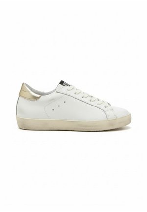 Witte lage sneaker met beige zool en gouden hieltab, uitgevoerd met veters aan de voorkant en kleine ventilatiegaatjes aan de zijkant.