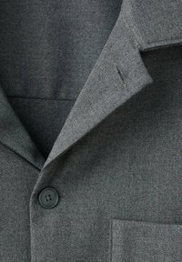 Blazer de tejido texturizado gris con solapa de muesca, cierre de un solo botón y un bolsillo en el pecho con detalles de costura sutil.